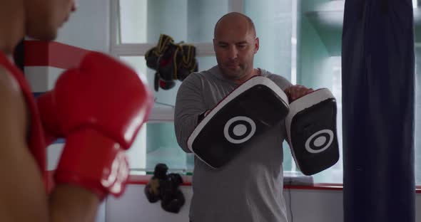 Caucasian man training with coach in boxing gym alt