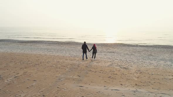 Young Couple Walking Towards Sunset On Beach