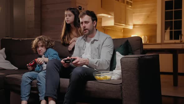 Father Playing with His Son in Game Console Laughing and Fighting on the Couch alt