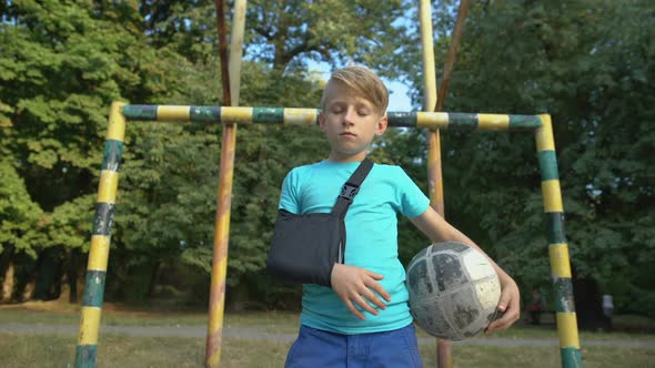 Upset Boy Wearing Shoulder Immobilizing Sling for Injured Arm, Holding Football