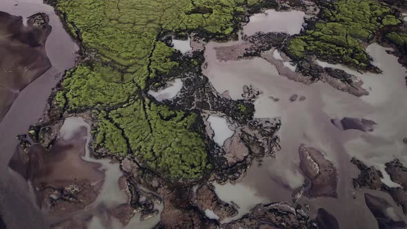 Drone Titling Up Over Braided River in Green Lava Field Landscape alt