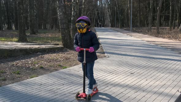 A little girl rides through the Park in the spring on a scooter in a protective helmet