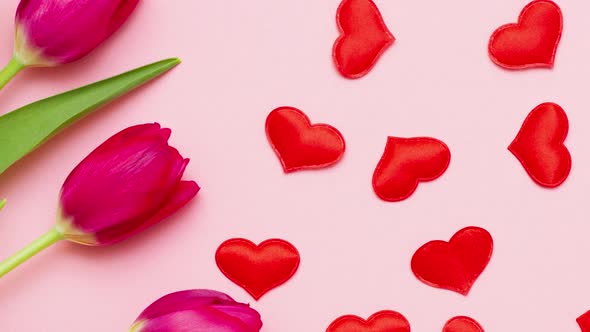 Bouquet of Red Fresh Juicy Tulips with Green Leaves Lie on Pastel Pink Background with Toy Hearts alt