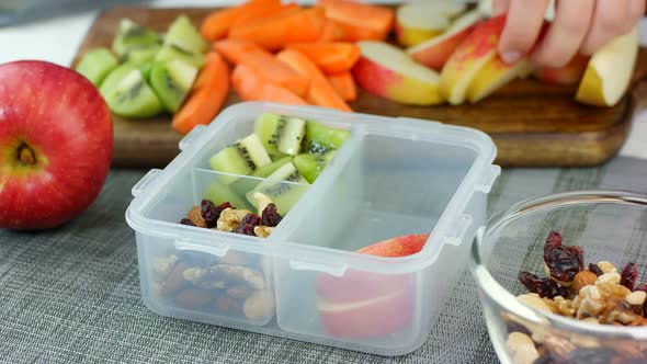 Woman hand put healthy fruit and nut snacks into the lunch box and close it