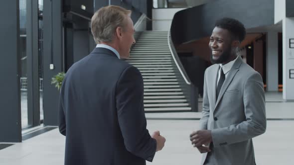 Two Diverse Friendly Businessmen Chatting in Office Hallway alt