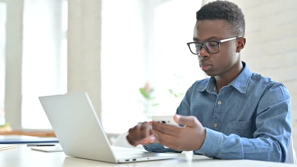 Focused Young African Man Using Laptop and Smartphone in Office alt