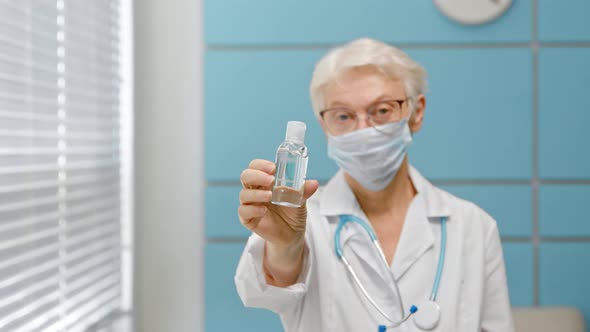 Skilled female doctor with glasses and protective mask stands in light hospital office alt
