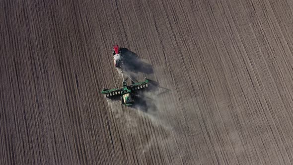 Aerial view of tractor with harrow system plowing ground on cultivated farm field alt