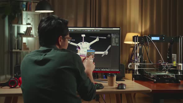 Back View Of Asian Engineer Using Mobile Phone While Work On Personal Computer And 3D Printer alt
