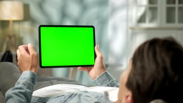 View From the Shoulder of Man Holding and Using Hand Gestures on Green Mock-up Screen Digital Tablet alt