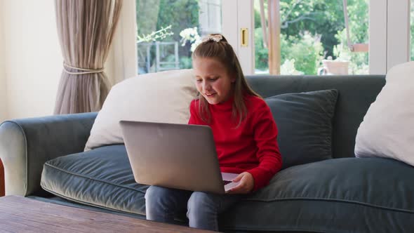 Caucasian girl using laptop while sitting on the couch in the living room at home alt