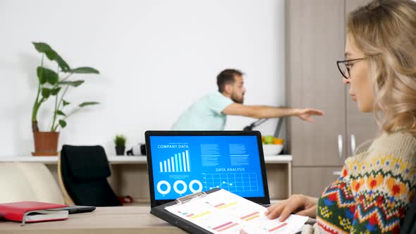 Woman at the Laptop Looking at Company Data Analysis and on Charts While Her Husband Is Making Noise alt
