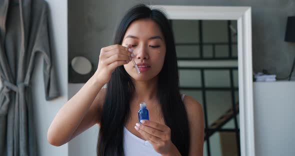 Beautiful Asian Woman Holding a Jar with Moisturizing Serum or Massage Oil and Applying Some Drops alt