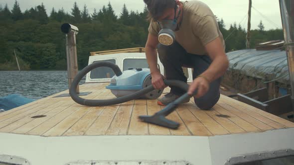 Young carpenter hoovering sanded wooden boat roof. MEDIUM WIDE SHOT alt