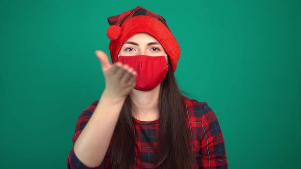 Woman Wearing Christmas Red Hat and Medical Protective Face Mask Looks Into Camera and Sends an Air