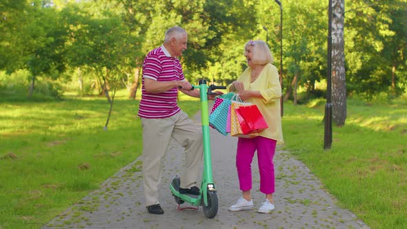 Senior Stylish Couple Grandmother Grandfather After Shopping with Bags Using Scooter for Riding alt