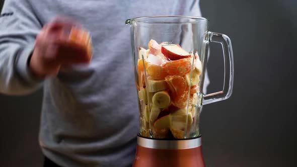 A man makes a nutritious fresh homemade fruit cocktail on an electric blender. alt