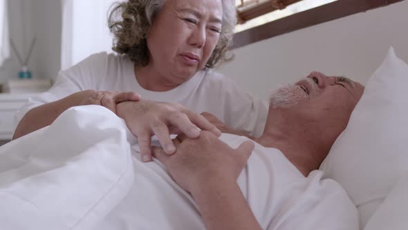 Asian elderly couple in bed, man's heart aches due to heart disease.
