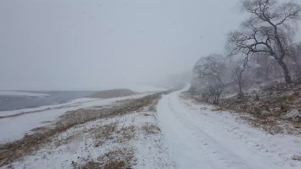 Country road between the frozen lake and leafless forest