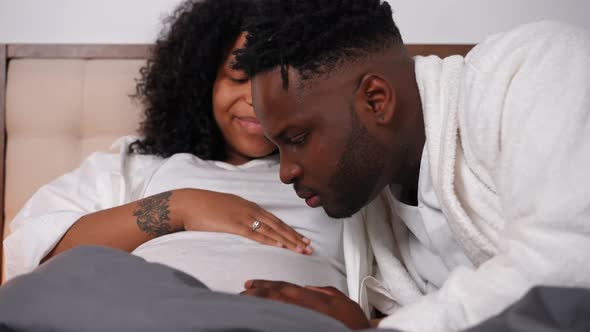 Happy Confident Young Father Kissing Pregnant Belly Listening Fetus Talking to Spouse alt