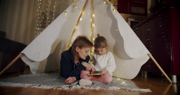 Happy Woman with Her Daughter at Smiling and Talking in Tent  Using Tablet alt