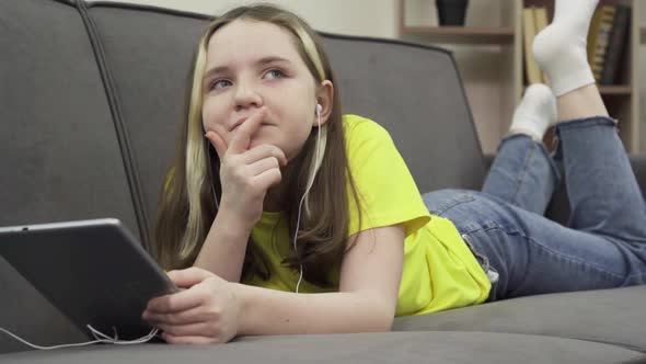 A Happy Millennial Caucasian Teenage Girl Lying on a Comfortable Couch Listening to Music on a alt