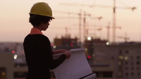 Architect holding plans looking at construction site at sunset