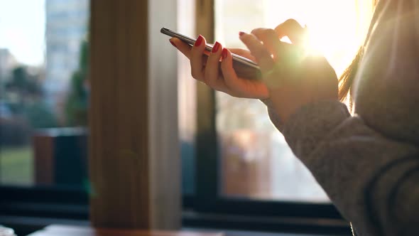 Female Hands Using Smartphone Against a Blurred Cityscape in the Setting Sun alt