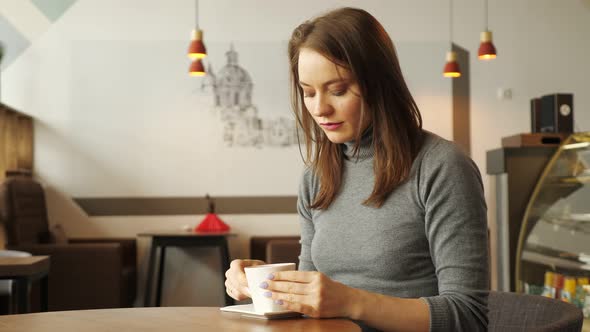 Women is Drinking a Cup of Coffee Sitting in Cafe alt