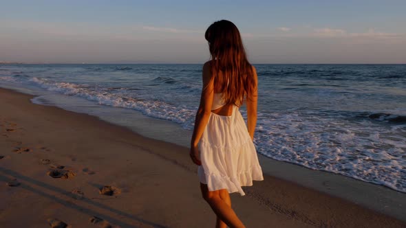 Beautiful woman in a white dress at the beach at sunset alt