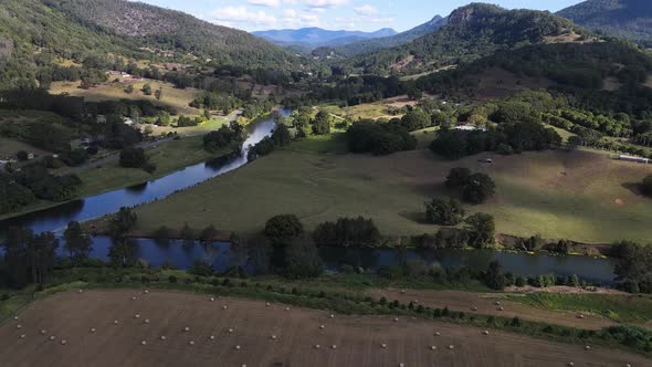 A high view drone video flying over farm land and along a small river through a scenic valley close alt