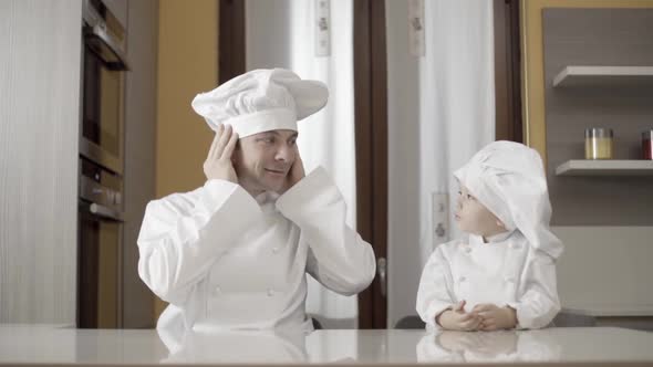 Dad Fix the Chef's Hat While His Son Looking at Him