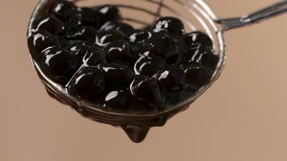 Close up on Steel Spoon with Sticky Black Tapioca Pearls Falling, Soft Background alt