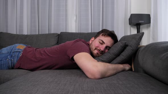 Happy young caucasian man takes a nap on a sofa in a modern apartment. alt