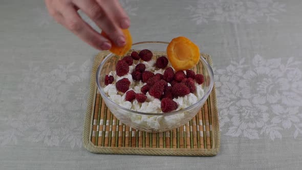 A Woman's Hand Places Apricot Slices in a Bowl of Cottage Cheese and Raspberries