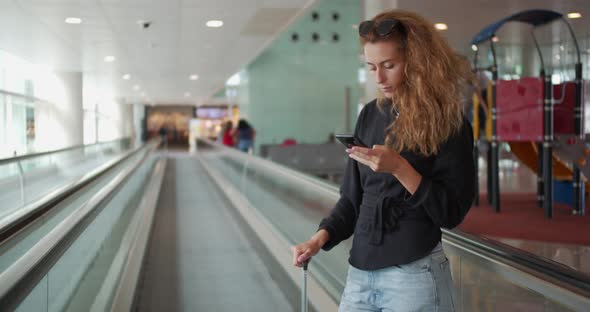 Woman on Escalator and Using Cellphone with Her Luggage in International Airport. alt