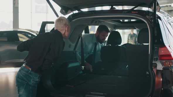 Car Salesman Showing Customer Car in Automotive Dealership Showroom alt