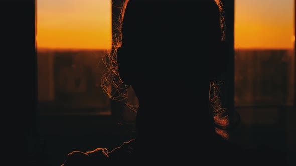 Silhouette of Young Woman Goes to the Window at Sunset Rear View Slow Motion alt