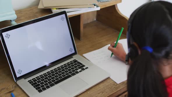 Mixed race girl at home in online school class, using headset and laptop with copy space on screen alt