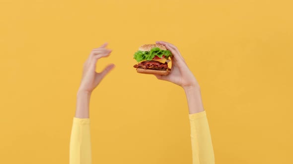 Hands holding and pointing to hamburger  on yellow studio background
