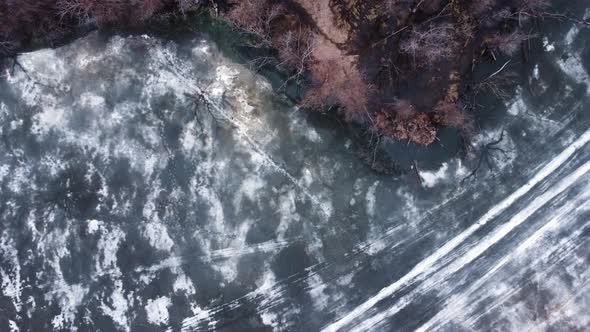 Aerial top down view of a lake with thin melted ice on the surface.