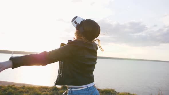 Portrait of Young Woman Having Some Fun in Vr Glasses Outdoors with Beatiful Sea Sunset Background alt