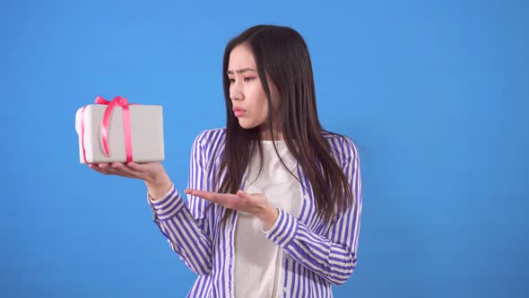 Dissatisfied with a Small Gift Young Sian Woman on a Blue Background alt