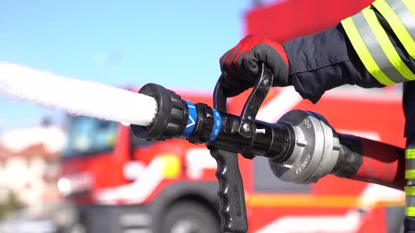 A firefighter is using fire hose for extinguishing fire.  Red and fire truck background