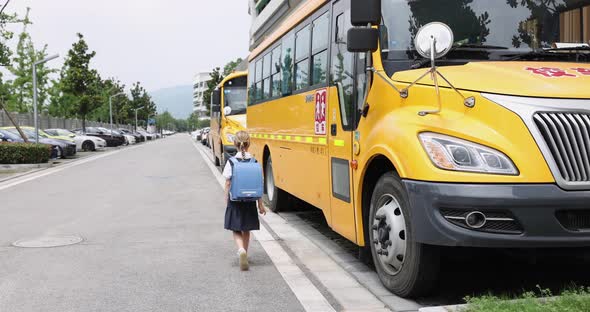 Schoolgirl Wearing School Uniform and Backpack and Standing Near Yellow Bus alt