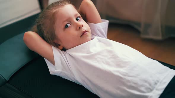 Tired Toddler in Sportswear Lies on Treadmill in Light Room alt