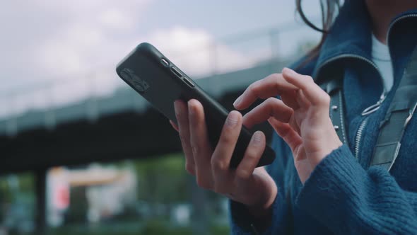 Young woman typing into her phone then looking around for directions alt