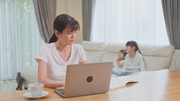 Asian busy Female freelance worker work at home due Covid-19 lockdown with young little kid. alt