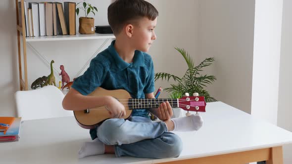 Talented Kid Playing Soprano Ukulele Sitting on Desk