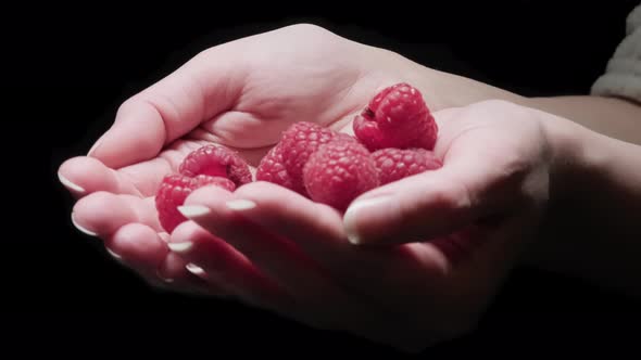 Female hands show delicious ripe raspberries on a black background.